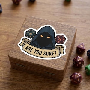 May include: A sticker featuring a dark hooded figure with glowing yellow eyes, flanked by two twenty-sided dice. Below the figure, a beige scroll banner displays the text ARE YOU SURE? in black capital letters. The sticker is on a wooden box.
