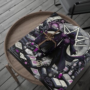 May include: A wrapped gift with a brown ribbon sits on top of a sheet of wrapping paper. The wrapping paper and gift feature a dark, gothic illustration with purple accents, including a robed figure, pentagrams, and books. Gold scissors are also visible.