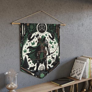 Puede incluir: Un tapiz de pared que representa a un arquero de fantasía con arco y flecha, rodeado de elementos forestales y dados. El diseño utiliza verde, marrón y negro, con una barra de madera y una cuerda para colgar.