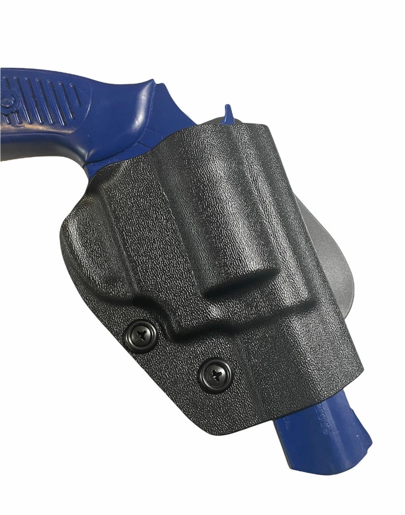 May include: Black, textured holster with two black screws, holding a blue handgun. The holster is designed to securely hold the firearm. The image is set against a white background.