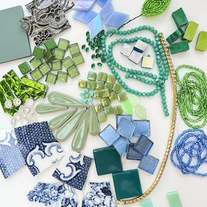 May include: An assortment of craft supplies in shades of green, blue, and white. Includes mosaic tiles, beads, decorative leaves, and patterned ceramic pieces. A variety of textures and shapes are visible, ideal for crafting and DIY projects.