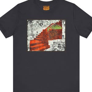 Peut inclure: Un t-shirt gris anthracite à manches courtes avec un imprimé rectangulaire central. Le motif représente un escalier rouge montant, une créature ressemblant à un lézard vert et des motifs abstraits complexes en noir et blanc.