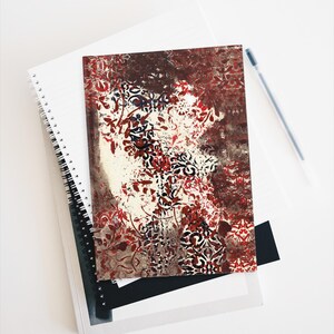 Op de afbeelding: Een notitieboekomslag met een abstract bloemenpatroon in rood, wit en zwart. Het patroon doet denken aan een vintage behang.