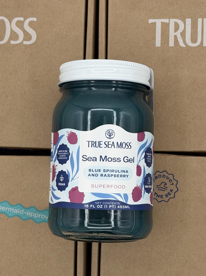 May include: A glass jar filled with dark teal sea moss gel, topped with a white lid. The label reads True Sea Moss, Sea Moss Gel, Blue Spirulina and Raspberry, Superfood, and Net Contents 16 FL OZ (1 PT) 453ML, featuring illustrations of raspberries.