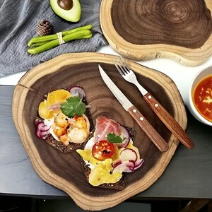 May include: Two open-faced sandwiches on a wooden serving platter. One sandwich has shrimp, the other has ham and a tomato. Both sandwiches have a creamy spread, radish, and cilantro.