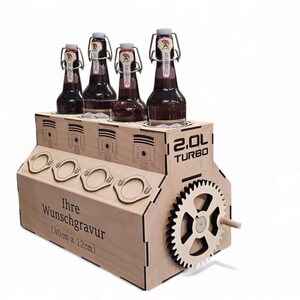 May include: A wooden beer bottle holder shaped like an engine block, holding four brown bottles. The holder has a gear and the text "2.0L TURBO". The front has the text "Ihre Wunschgravur (40cm x 12cm)".