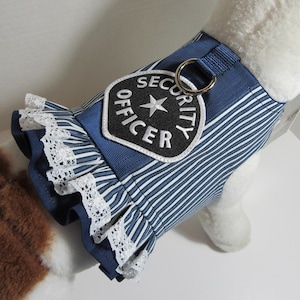 May include: A blue and white striped pet harness with a white lace trim and a "SECURITY OFFICER" patch. The harness has a metal ring and is designed to fit a small dog or pet.