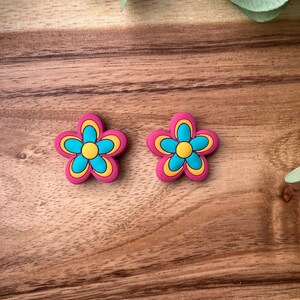 Peut inclure: Deux breloques en forme de fleur rose avec des centres jaunes et bleus. Les breloques sont faites d'un matériau souple et flexible et ont une finition brillante.