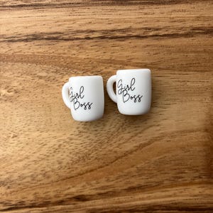 Peut inclure: Deux tasses en céramique blanche avec l'inscription "Girl Boss" en noir.