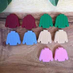 Peut inclure: Dix petits charmes en silicone en forme de pull, de différentes couleurs, dont le rouge, le vert, le bleu, le beige et le rose.