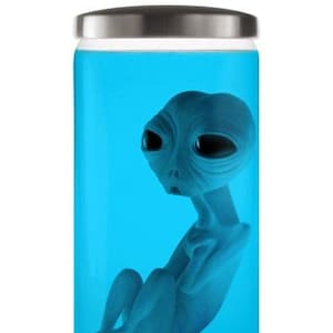 Puede incluir: Una figura alienígena azul dentro de un frasco de vidrio transparente lleno de líquido azul. El alienígena tiene una cabeza grande, ojos negros y está sentado. El frasco tiene una tapa plateada.