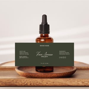 Può includere: Flacone di vetro marrone di siero per il viso con contagocce nero, posto su un vassoio di legno. L'etichetta verde scuro recita "Face Serum daily glow". Il flacone contiene 30 ml.