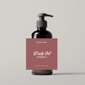 May include: A dark brown glass bottle with a black pump dispenser. A square label in a muted red colour is affixed to the bottle, with the words "Body Oil daily glow" in white script. The label also includes the text "10 ml | 0.33 fl oz".