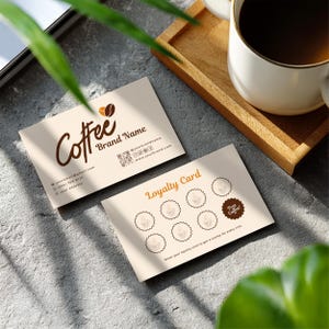 Puede incluir: Dos tarjetas de visita beige con temática de café. Una tarjeta presenta la palabra "Coffee" en escritura cursiva, un gráfico de grano de café e información de contacto. La segunda tarjeta es una tarjeta de fidelización con iconos de tazas de café y el texto "Loyalty Card".