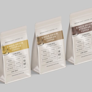 Op de afbeelding: Drie witte koffiezakken met verschillend gekleurde etiketten, elk met het opschrift "Single-Origin Ethiopian Coffee". De zakken hebben een koffiekopje-logo en smaaknotities.