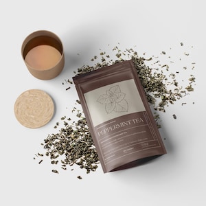 May include: A brown pouch of peppermint tea with a botanical illustration and the text "Peppermint Tea." Loose tea leaves surround the pouch, a small cup, and a coaster. The cup contains a light brown liquid.