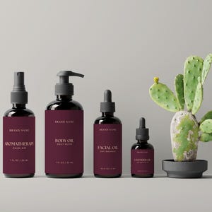 May include: Aromatherapy, body oil, facial oil, and lavender oil bottles with dark burgundy labels and black caps. A potted cactus is to the right. The bottles are arranged in a row. The aromatherapy bottle is 1 fl oz / 30 ml.
