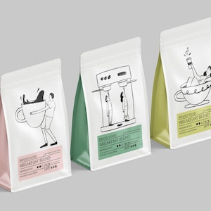 Op de afbeelding: Drie witte koffiebonenzakken met illustraties en tekst. De zakken hebben verschillende gekleurde accenten: roze, groen en geel. Elke zak heeft een unieke zwart-wit tekening van mensen en koffiekopjes. De tekst luidt "Breakfast Blend".