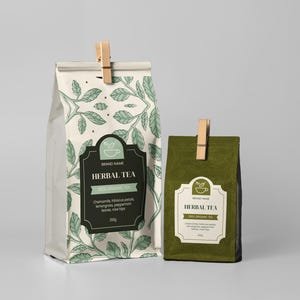 Könnte beinhalten: Zwei Kräuterteetüten, eine große und eine kleine, mit Holzklammern. Die größere Tüte ist weiß mit einem grünen Blättermuster und einem schwarzen Etikett mit der Aufschrift "Herbal Tea". Die kleinere Tüte ist olivgrün.