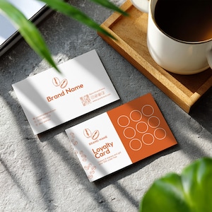 May include: Two business cards with a coffee bean logo and the words "Brand Name" and "Loyalty Card". One card has a QR code and social media icons. The other card has a design of circles. A cup of coffee sits on a wooden tray.