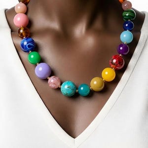 May include: A multi-colored beaded necklace featuring spherical beads in various shades including pink, blue, green, yellow, purple, and orange. The beads have different finishes, ranging from solid opaque colors to marbled and translucent textures, strung together on a thin cord.
