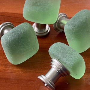 May include: Four green glass cabinet knobs with a silver base. The knobs have a textured, frosted finish.