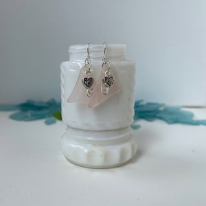May include: A pair of pink glass earrings with silver heart charms. The earrings are hanging from a white surface.
