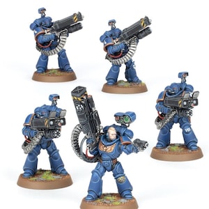 May include: Five miniature figures of Space Marines in blue armor, each holding a large black weapon with a silver ammunition belt. The figures stand on brown bases. One figure has a bald head and is holding a smaller black weapon.