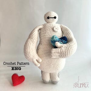 May include: White crochet amigurumi toy of Baymax from the movie Big Hero 6. The toy is holding two blue and white crocheted hearts. The toy is standing on a white surface. Crochet Pattern ENG