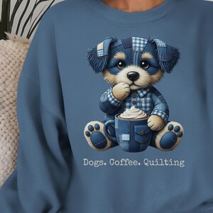 May include: A blue sweatshirt featuring a cartoon dog wearing a patchwork outfit and holding a coffee cup with whipped cream. The text "Dogs. Coffee. Quilting" is printed below the image.
