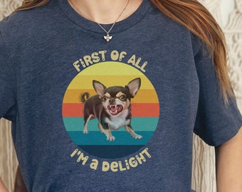 May include: A navy blue t-shirt with a vintage-style graphic of a chihuahua with the text "First of all I'm a delight".