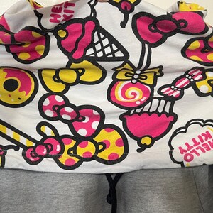 May include: A gray hoodie with a white hood featuring a colorful pattern of donuts, bows, ice cream cones, and candy. The hood design includes the text "HELLO KITTY" in a cloud-shaped design.
