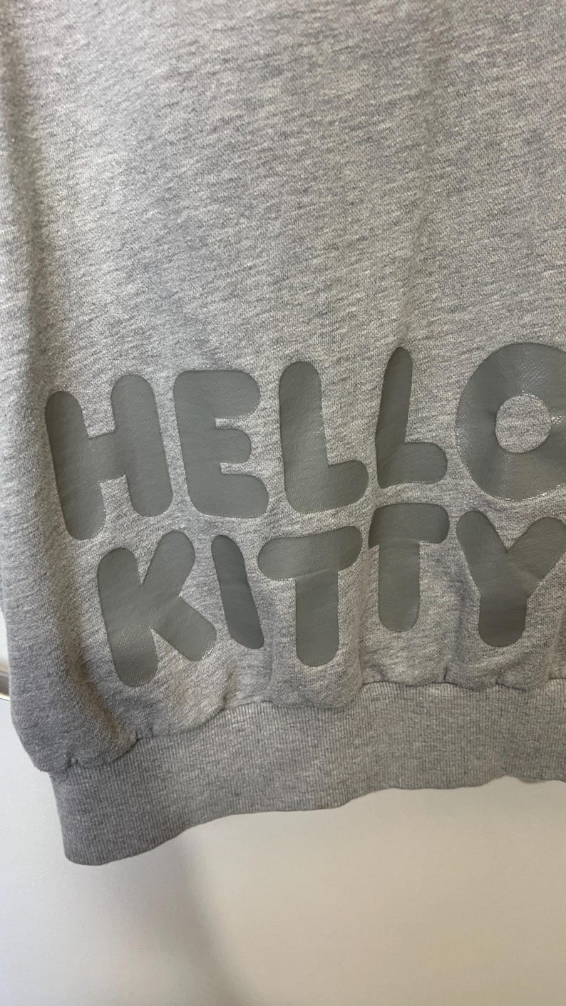 May include: A gray sweatshirt with the words "HELLO KITTY" in large, gray, block letters across the front. The sweatshirt has a ribbed hem and cuffs.