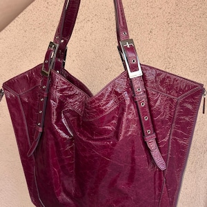May include: A large, burgundy leather tote bag with silver buckles and a zipper closure.