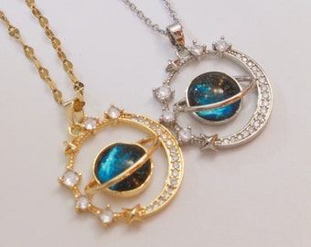 May include: Two necklaces with a galaxy-themed pendant. One necklace is gold with a blue and black galaxy pendant, and the other is silver with a blue and black galaxy pendant.