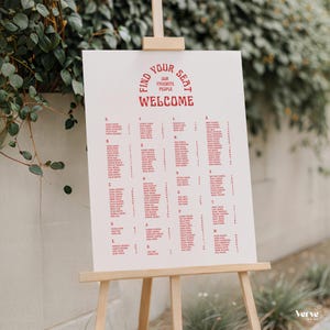Puede incluir: Un letrero de bienvenida blanco sobre un caballete de madera. El letrero tiene texto rojo que dice: "Find Your Seat, Our Favorite People, Welcome." Debajo del texto hay listas de nombres, probablemente para una boda o evento.