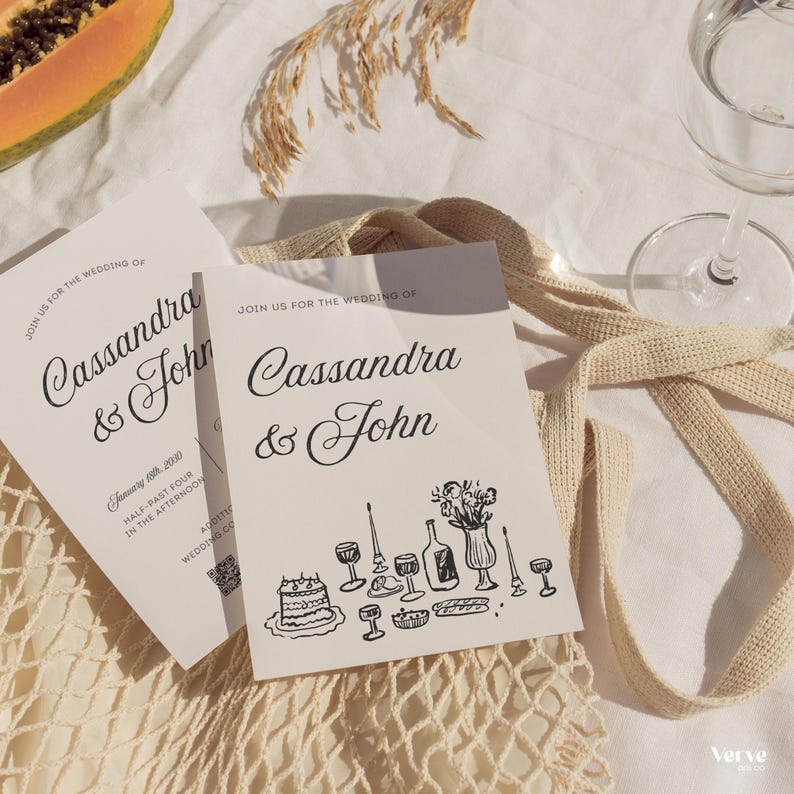 May include: Two wedding invitations with the names "Cassandra & John" in elegant script. The invitations are white with black text and illustrations of wedding-related items. A glass of water and a beige tote bag are also in the image.