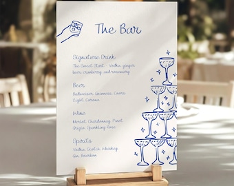 Könnte beinhalten: Eine weiße, rechteckige Barkarte in einem hellen Holzständer mit blauen Strichzeichnungen einer Hand, die ein Glas hält, und einem Champagnerturm. Der Text lautet The Bar, Signature Drink, The Sweet Start, Beer, Budweiser, Guinness, Coors Light, Corona, Wine, Merlot, Chardonnay, Pinot Grigio, Sparkling Rose, Spirits, Vodka, Scotch, Whiskey, Gin, Bourbon.