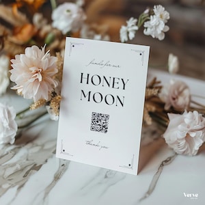 Può includere: Una carta bianca con le parole "Funds for our HONEYMOON" in corsivo nero e un codice QR. La carta è decorata con decorazioni agli angoli e circondata da fiori bianchi e color pesca.