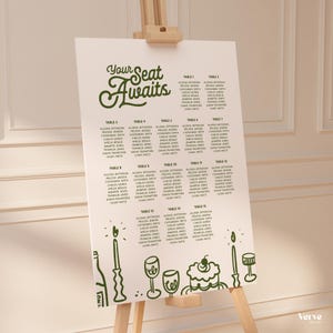 May include: A white seating plan displayed on an easel, featuring the green text "Your Seat Awaits". The plan lists names under tables 1-15. Green line drawings of candles, wine glasses, and a cake are at the bottom.