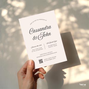 May include: A wedding invitation with the names Cassandra & John in elegant script. The invitation includes the date, time, and location: The Driskill Hotel in Austin, Texas. Additional details are available online. The invitation is held by a hand.