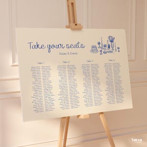 May include: A cream-colored wedding seating chart on a wooden easel. The chart features the text "Take your seats" and the names "Elaine & Lewis" in blue script. Four tables are listed with guest names.