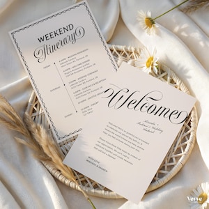 May include: Two cream wedding stationery cards with black text. One is a weekend itinerary, the other says "Welcome." The cards are in a woven basket with daisies and dried grass.