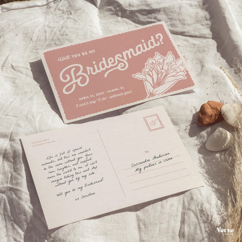 May include: Two pink postcards with the text "Will you be my Bridesmaid?" in a script font. One card has a floral illustration. The other card has handwritten text. The cards are on a white surface.