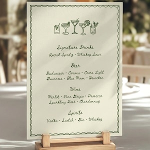 A cream-colored menu card with a hand drawn green border and drink illustrations. The menu lists signature drinks, beer, wine, and spirits. The card is held by a small, light-colored wooden stand.