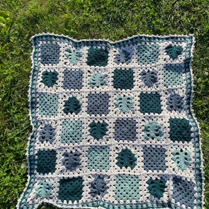 May include: A crocheted blanket with a granny square pattern in shades of green, blue, and white.