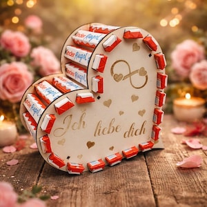 Könnte beinhalten: Eine herzförmige Holzbox gefüllt mit Kinder Riegel Schokoriegeln. Auf der Box steht "Ich liebe dich" und sie ist von rosa Rosen und Kerzen umgeben.