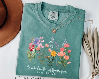 May include: A light green short-sleeve t-shirt with a graphic of colorful wildflowers and the white text "Consider how the wildflowers grow Luke 12:27-28". The shirt features a Comfort Colors brand label on the inside neck showing size S-P-CH.