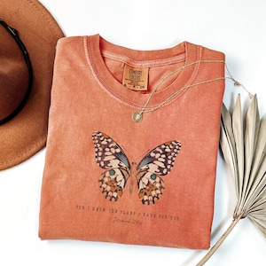 May include: A peach-colored t-shirt with a butterfly graphic and the text "For I know the plans I have for you, Jeremiah 29:11".