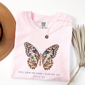 May include: Pink t-shirt with a butterfly graphic and the text "For I know the plans I have for you Jeremiah 29:11".